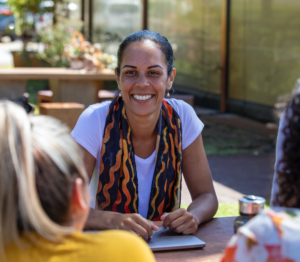 A woman smiles as she talks to several other women sitting across a table from her