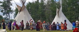 Large group in tribal attire standing infant of teepees