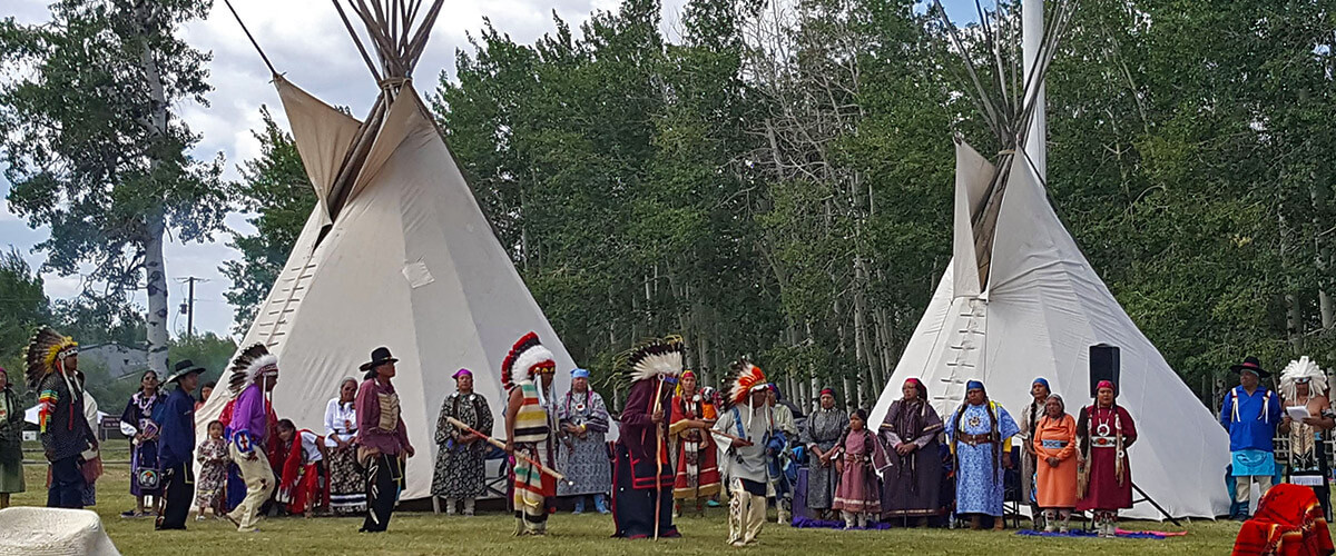 Large group in tribal attire standing infant of teepees