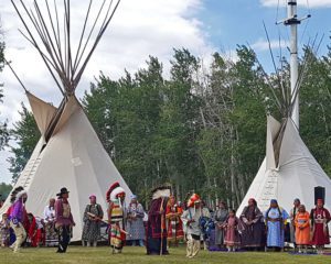 Large group in tribal attire standing infant of teepees
