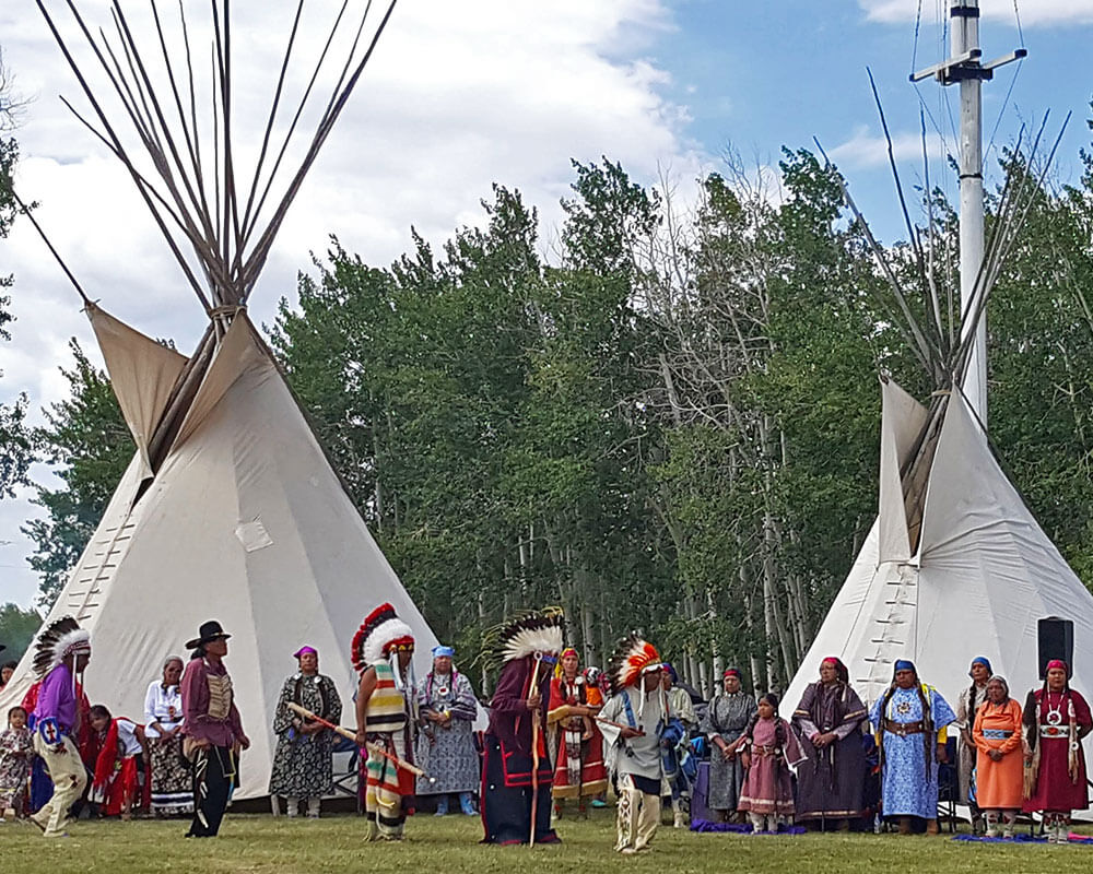 Large group in tribal attire standing infant of teepees