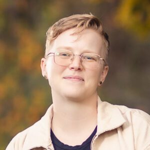 A headshot of a woman in her 30s with short blonde hair and glasses.